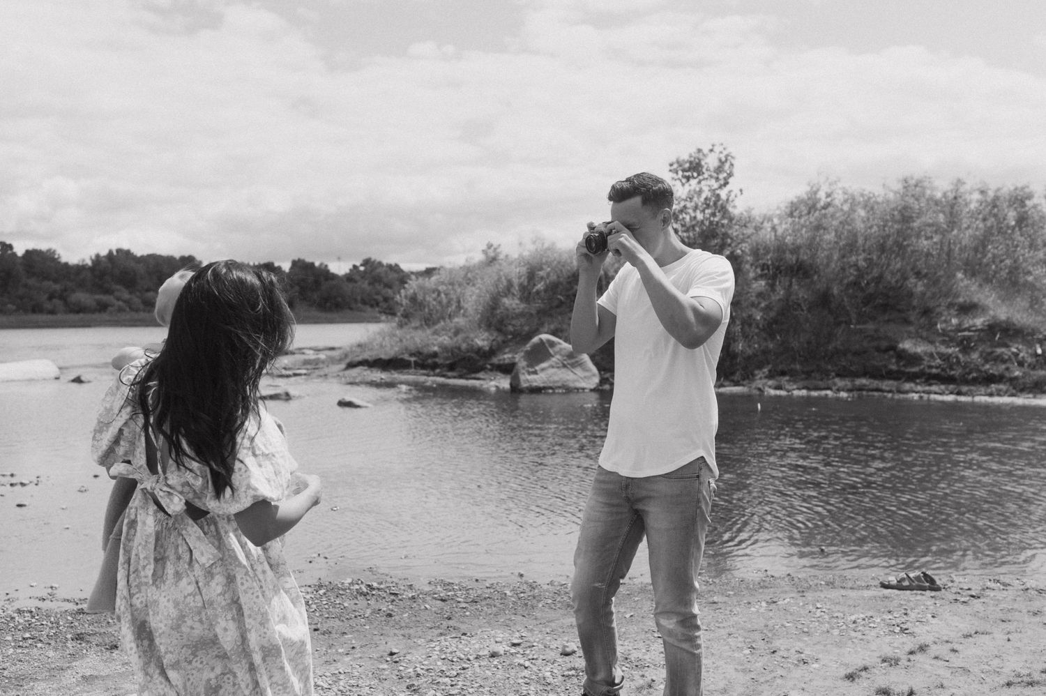Family enjoying playful moment by river in black and white photography.