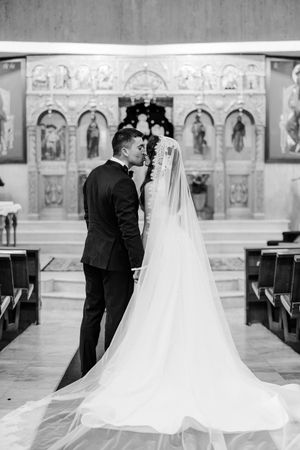 Black and white photo of bride and groom kissing at church altar, brides long veil trailing down aisle.