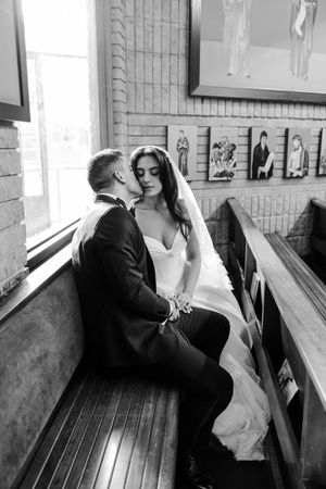 Black and white romantic portrait of bride and groom sharing intimate moment on church pew.
