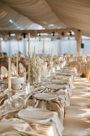 Luxurious wedding reception table with tall candles, white florals, and champagne satin linens.