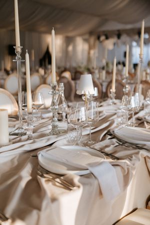 Elegant wedding reception table set with crystal glassware, white candles, and ivory satin linens.