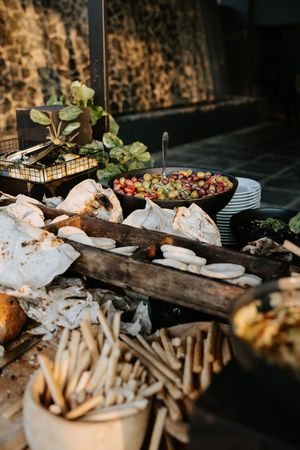 Rustic wedding grazing table with artisan breads, breadsticks, olives, and fresh garnishes on wooden board.