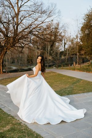 Bride twirling in a flowing white strapless ball gown on a garden path at golden hour during outdoor bridal portraits.