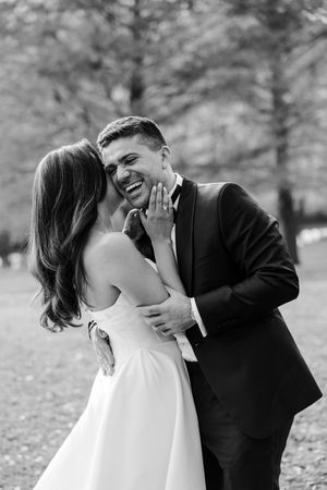 Black and white photo of laughing groom and bride sharing a joyful moment during wedding portraits.