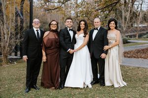Wedding couple poses with four family members outdoors in formal attire on their special day.
