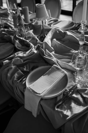 Black and white close-up of elegant wedding table setting with draped linen, plates, and candles.