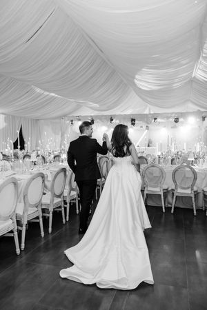 Black and white photo of bride and groom entering elegant wedding reception hall with draped ceiling.