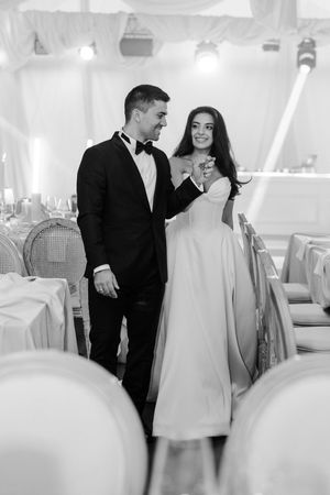 Black and white photo of elegant bride and groom sharing first dance in beautifully decorated reception hall.