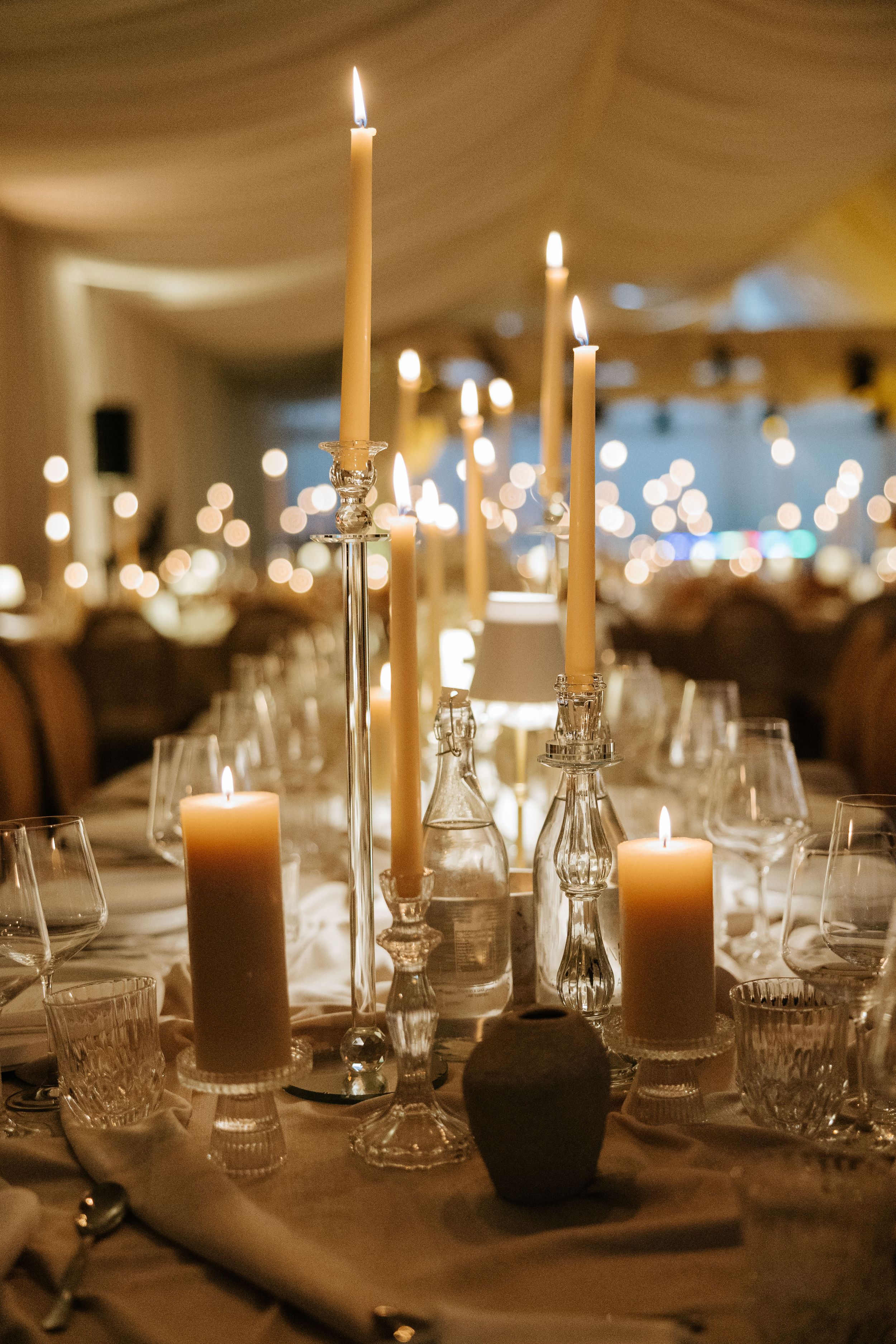 Elegant wedding reception table with tall ivory taper candles in glass holders and pillar candles creating warm ambiance.