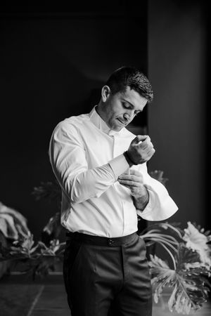 Black and white photo of groom fastening cufflinks while getting ready for his wedding ceremony.