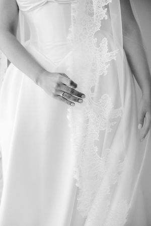 Black and white close-up of bride in white satin gown with lace veil detail at wedding.