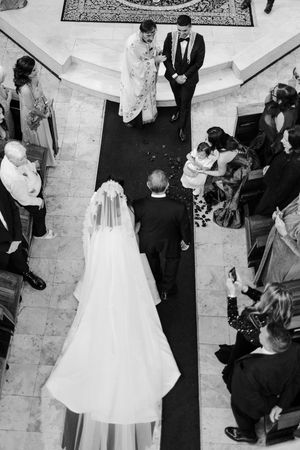 Aerial black and white view of bride walking down church aisle toward groom at wedding ceremony.