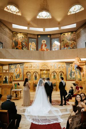 Bride and groom stand at ornate golden altar of Orthodox church with stunning Byzantine iconography.