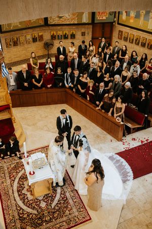 Aerial view of a wedding ceremony in an Orthodox church with guests seated in wooden pews.