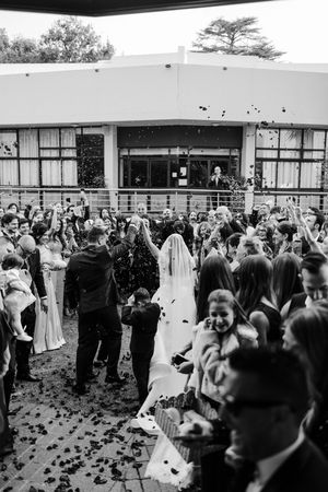 Black and white photo of newlyweds celebrating with confetti surrounded by cheering guests after ceremony.