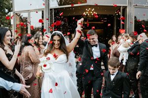 Joyful newlyweds exit church as guests shower them with red rose petals in celebratory send-off.