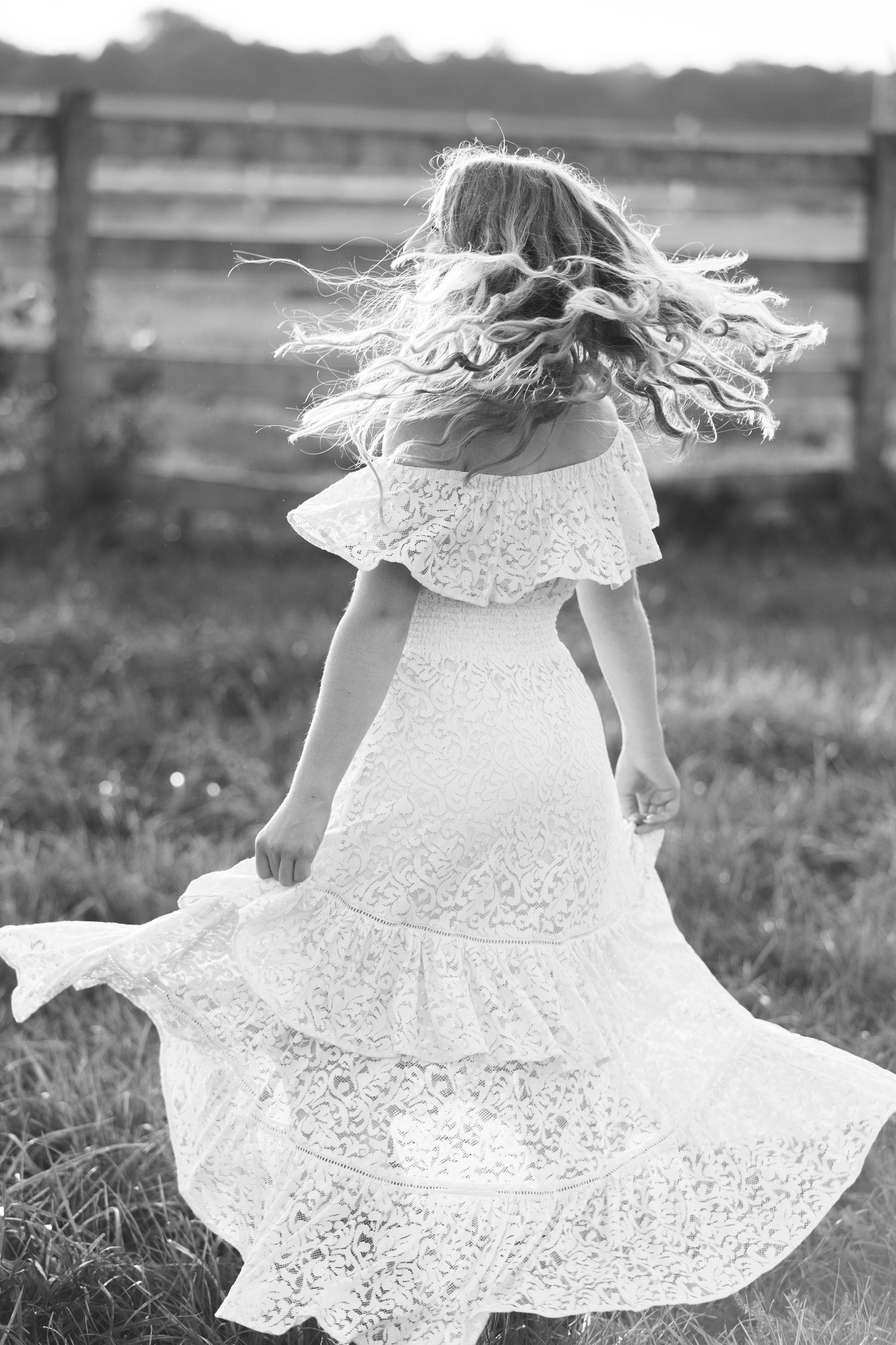 Black and white photo of a girl in a white lace dress twirling outdoors, her long hair flowing in motion.