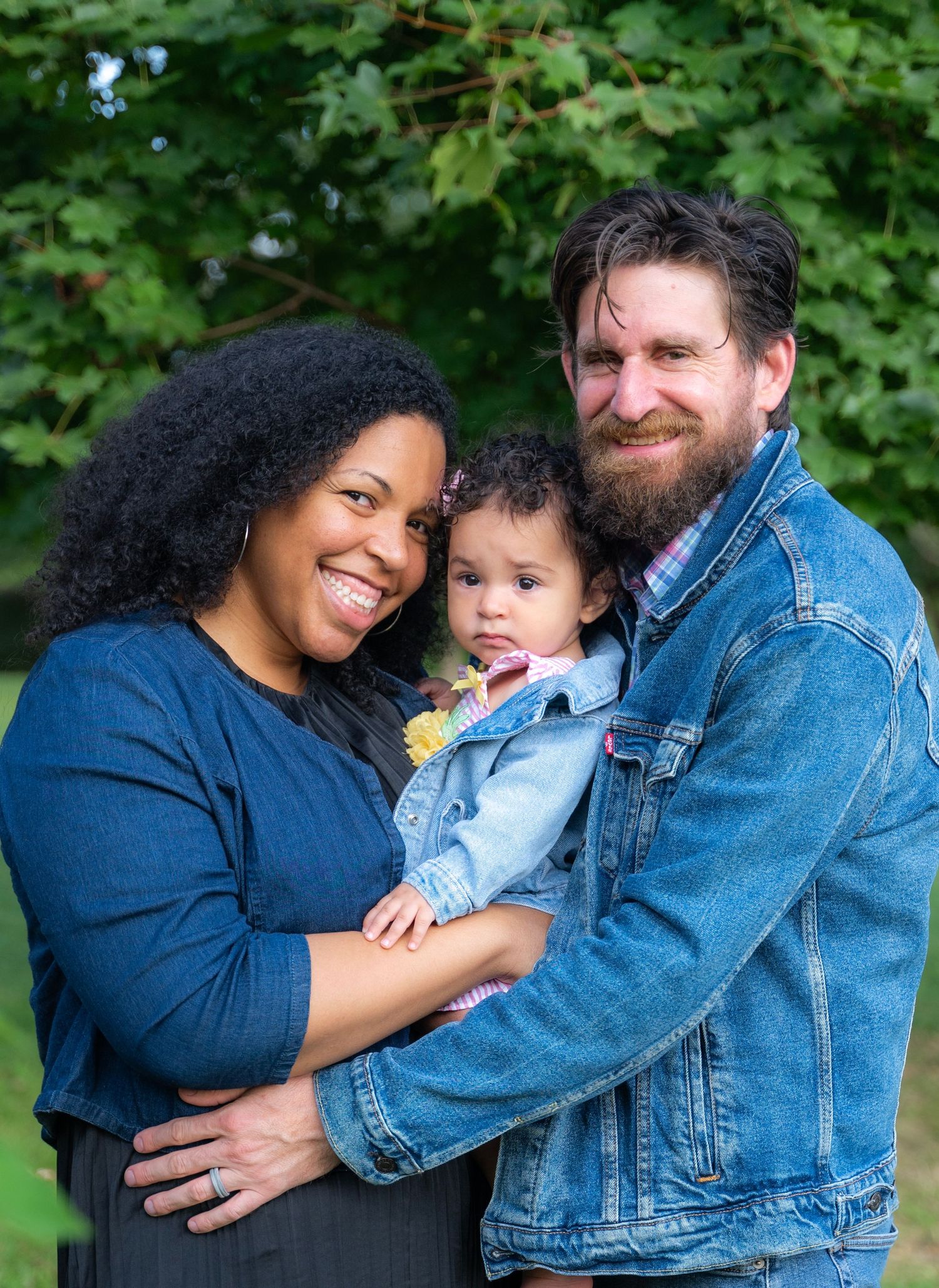 A family embraces while standing together in front of green foliage.
