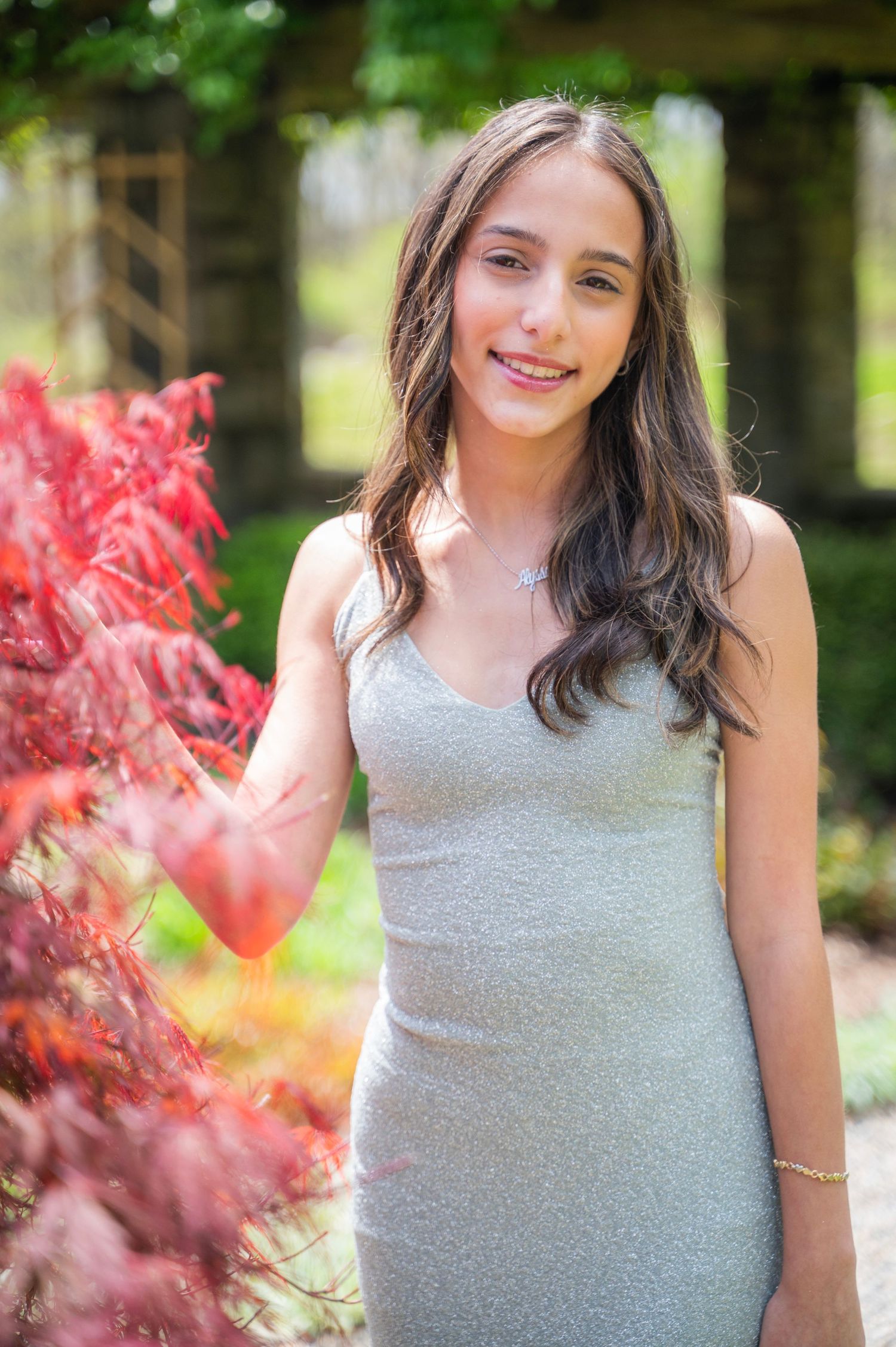 Young woman in grey dress poses in garden with red foliage.