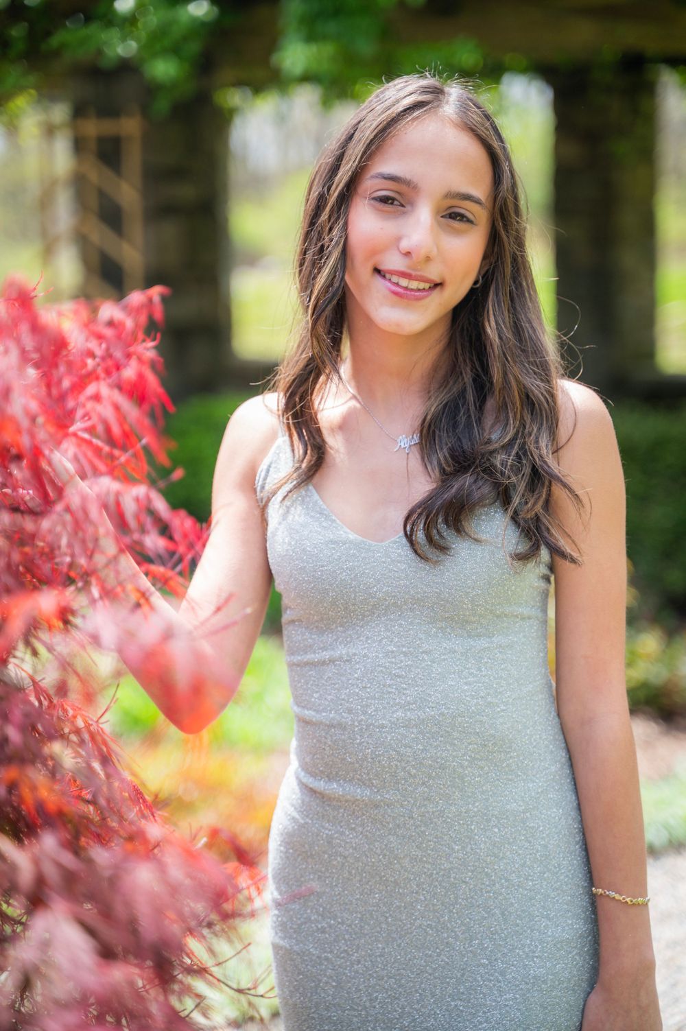 Young woman in grey dress poses in garden with red foliage.