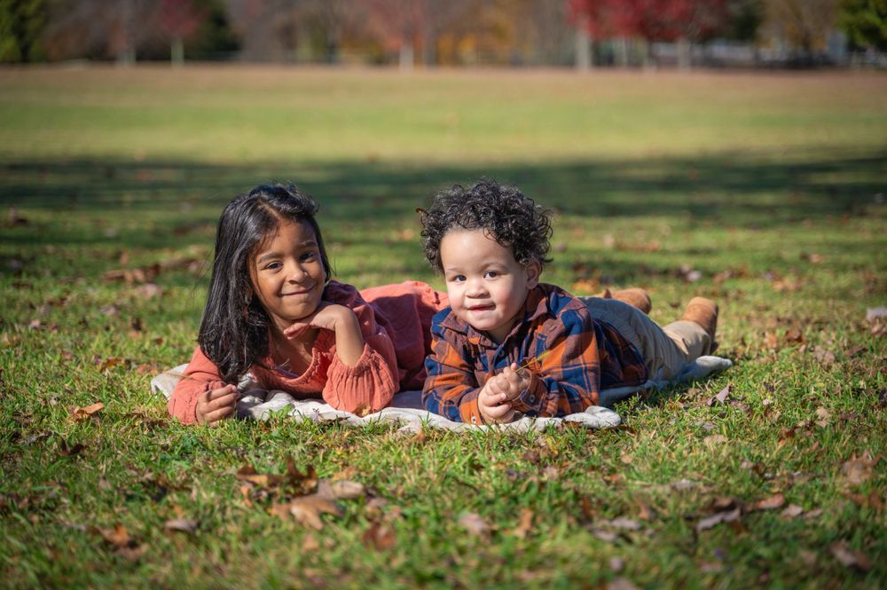 Group lounging outdoors on autumn grass surrounded by fallen leaves.