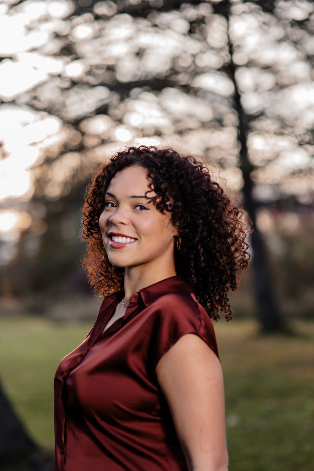 Outdoor portrait with natural bokeh lighting and burgundy top against a blurred forest background.
