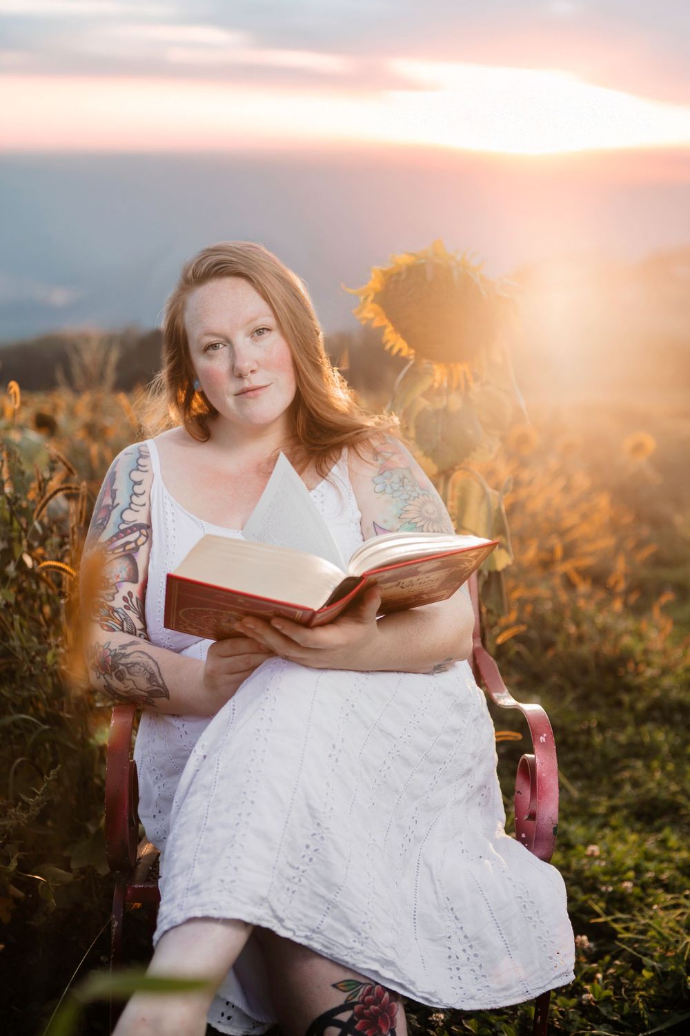 Person in white dress reading a book in a sunflower field at golden hour.