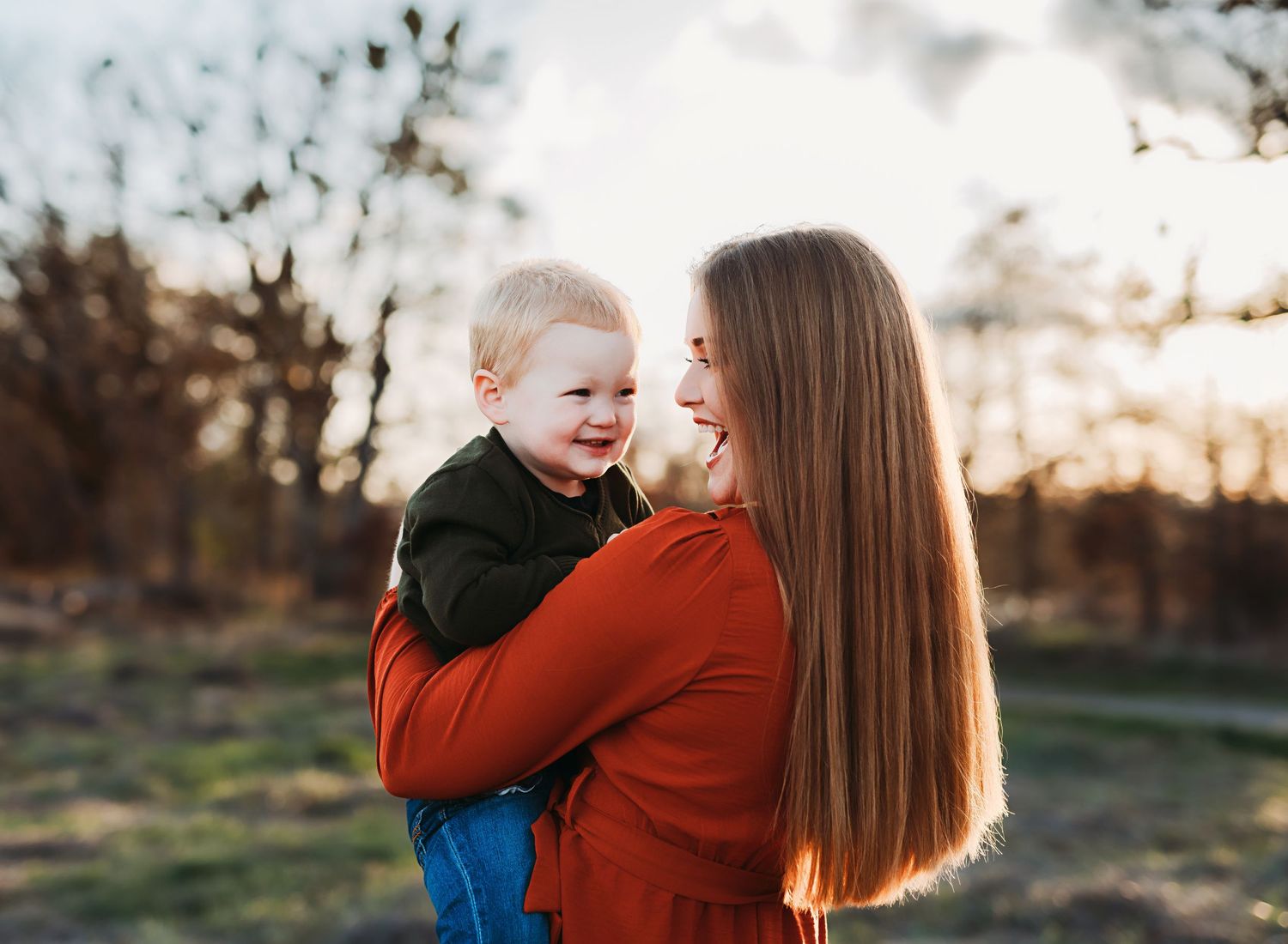 A joyful moment captured between parent and child outdoors during sunset with warm autumn colors in the background.