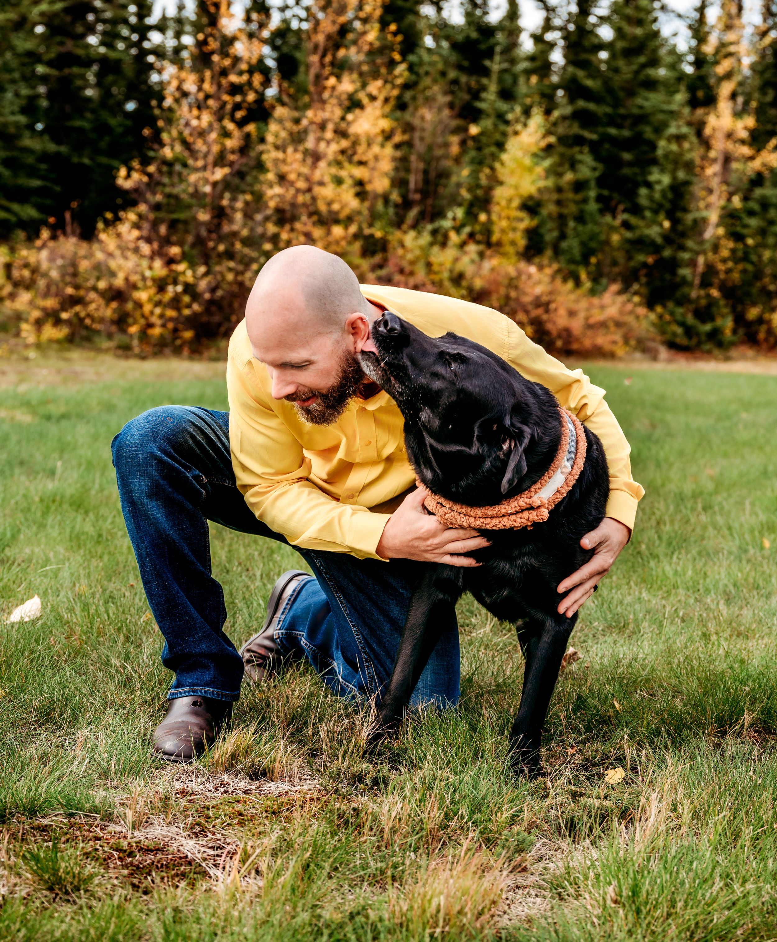 Black dog receives affectionate pets while wearing an orange bandana outdoors in autumn.