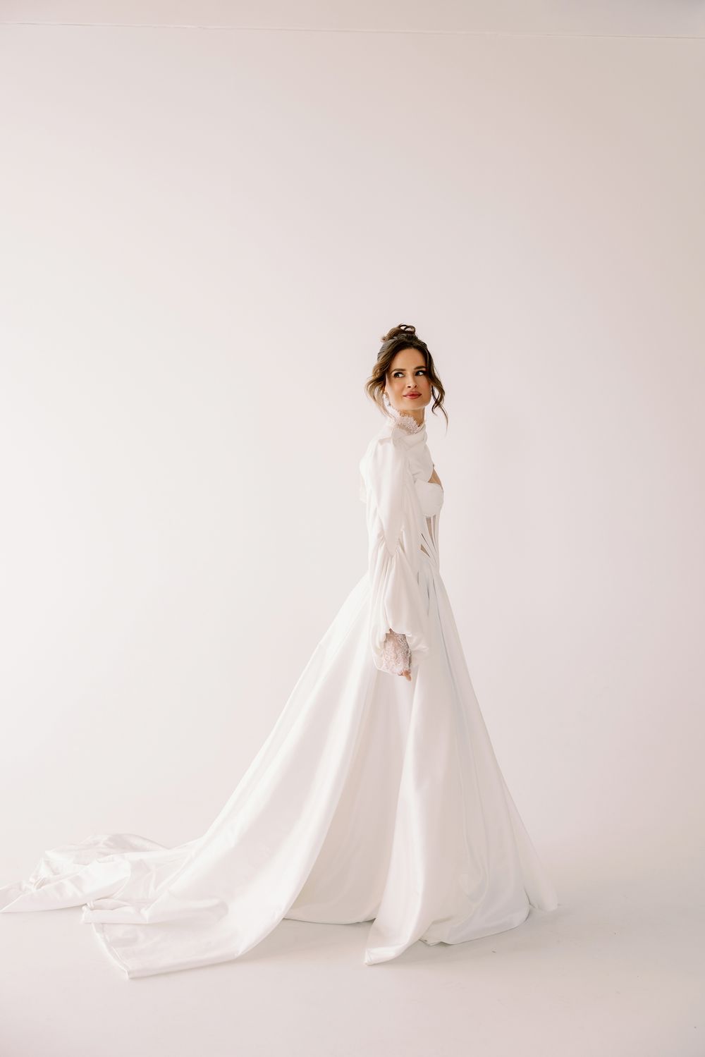 Elegant long-sleeved white wedding dress with flowing train photographed against minimalist light background.