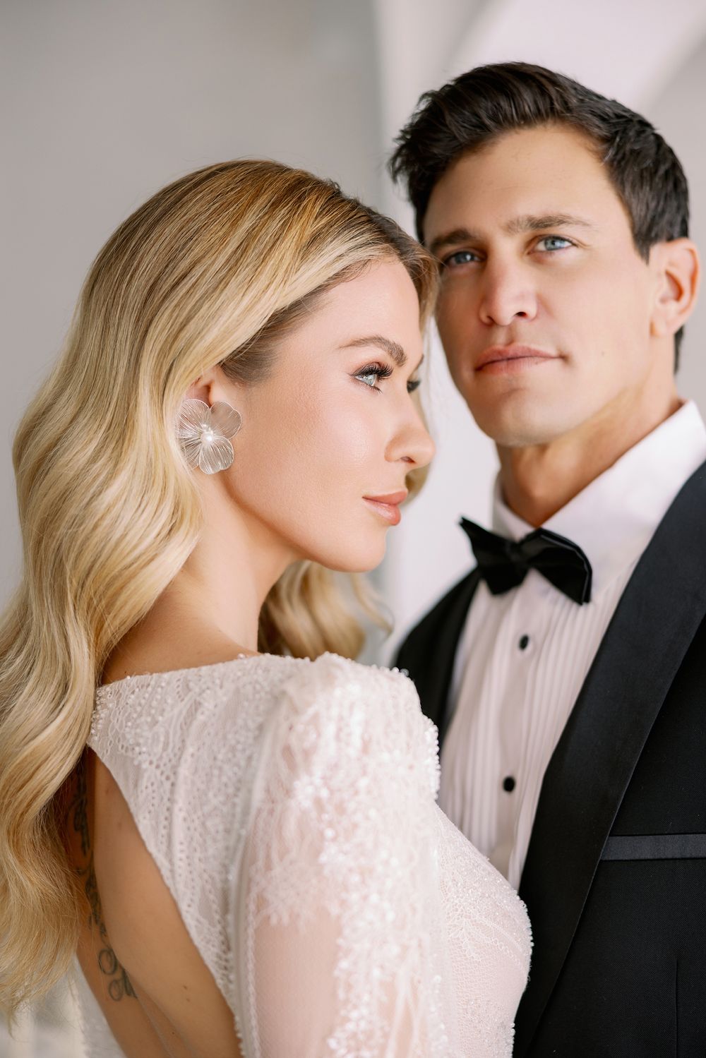 A bride in a beaded white dress and groom in black tuxedo pose for an elegant wedding portrait.