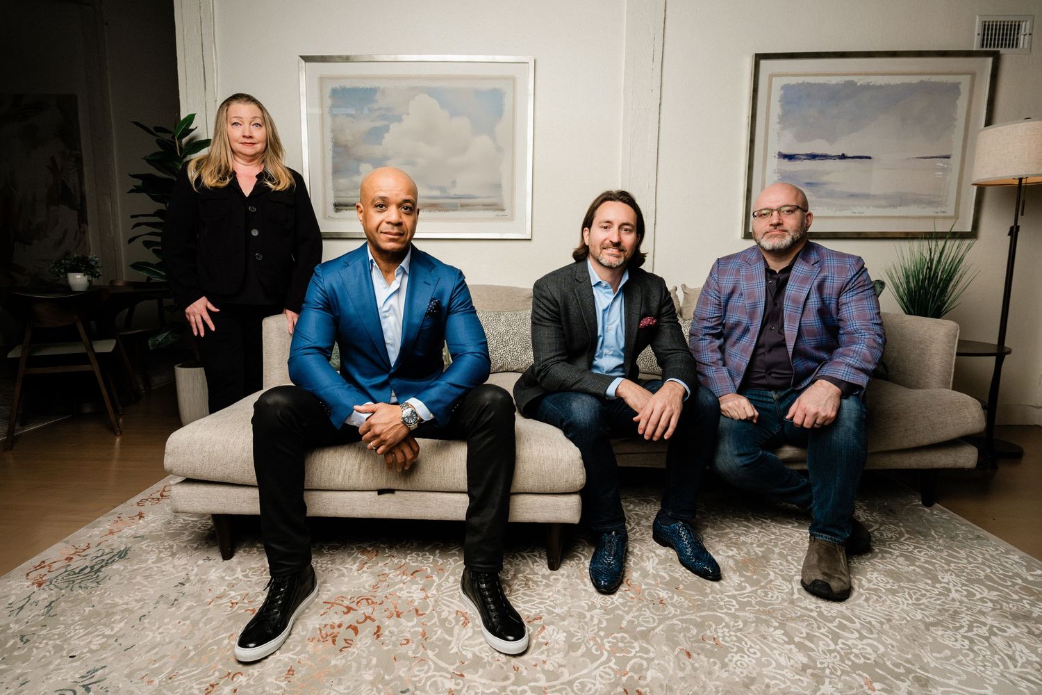 Four professionals pose on a beige sofa in a modern living room setting with artwork on the wall behind them.