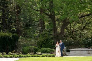 Bride and groom walking together through a lush green garden on their wedding day.
