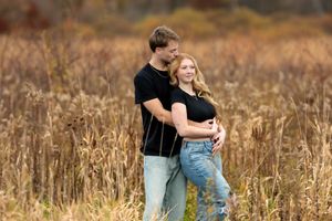 Couple embracing in tall golden grass field during fall engagement photography session.