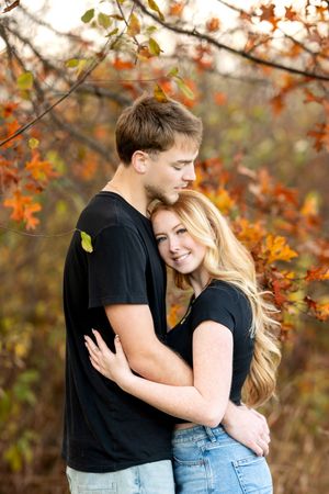 Couple hugging under vibrant orange autumn leaves during fall engagement photo session.
