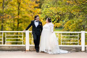 Bride and groom share a romantic moment on a white bridge surrounded by vibrant autumn foliage.