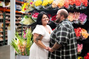 Couple smiling and holding hands near colorful flower displays during a unique Costco engagement session.