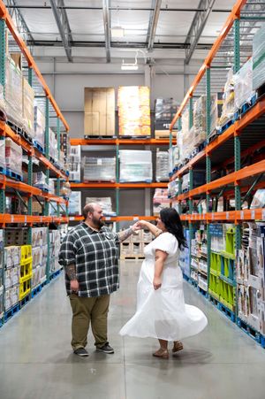 Couple dancing playfully in the wide aisles of a Costco warehouse during their engagement photos.