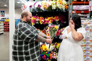 Man presenting colorful bouquet to surprised woman in Costco flower section.
