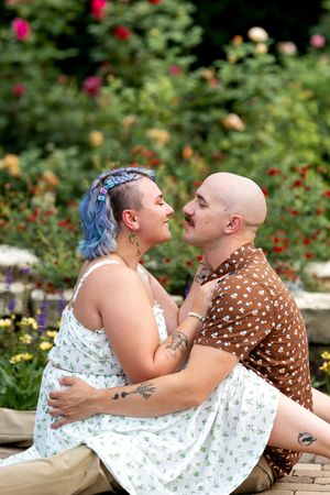 Couple sitting together in a colorful rose garden, gazing lovingly at each other in warm sunlight.