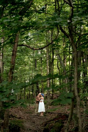 Couple embracing and kissing on a woodland path surrounded by lush green trees.