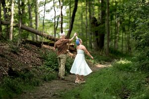 Couple dancing on a forest trail, woman in white dress with blue hair and man in brown shirt.
