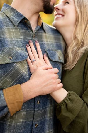 Couple sharing a tender moment, woman displaying engagement ring on man's chest in autumn setting.