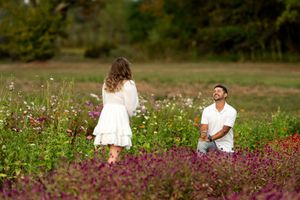 Romantic marriage proposal in a blooming wildflower field, man kneeling with ring as woman turns toward him.