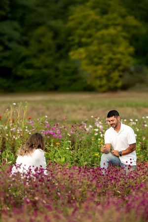 Man kneeling in a colorful flower field smiling up at woman during an outdoor marriage proposal.