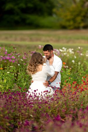 Newly engaged couple embracing and sharing a tender moment in a vibrant summer wildflower garden.