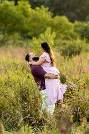 Man lifting his partner joyfully in a lush green meadow during a romantic outdoor couples session.