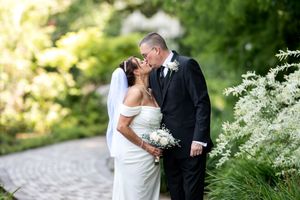 Newlyweds sharing tender kiss surrounded by lush greenery on wedding day.