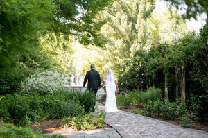 Bride and groom walking hand in hand through lush green garden pathway.