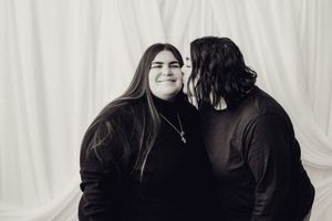 Black and white photo of a couple sharing a tender kiss on the cheek against a white backdrop.